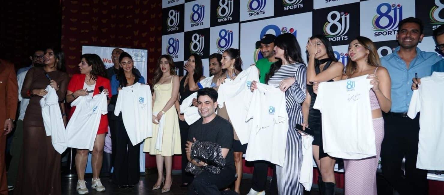 Fans celebrating at a cricket event with team merchandise, in front of a branded backdrop and large screen.